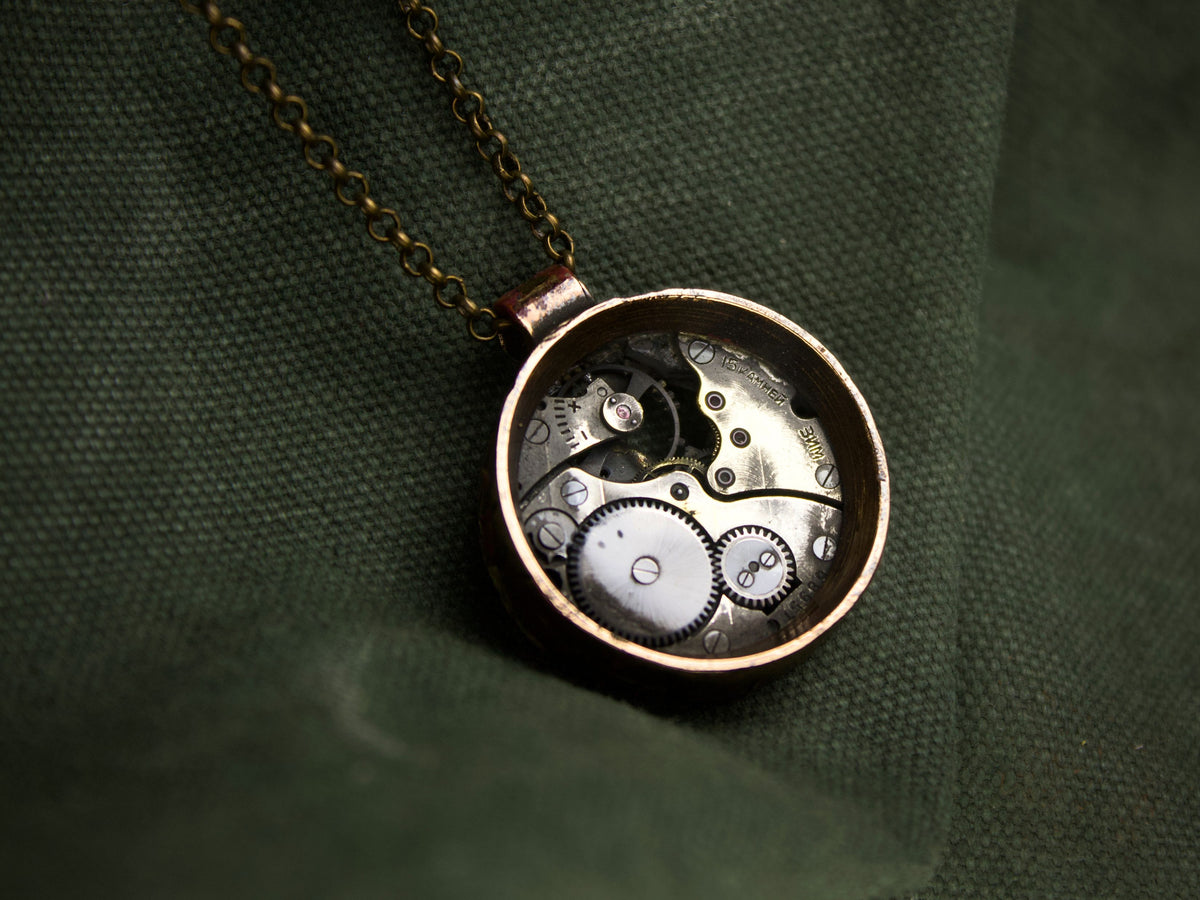 Collana con pendente rotondo in bronzo, contenente meccanismi di orologio con ingranaggi visibili e finitura grezza