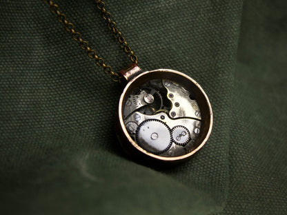 Collana con pendente rotondo in bronzo, contenente meccanismi di orologio con ingranaggi visibili e finitura grezza