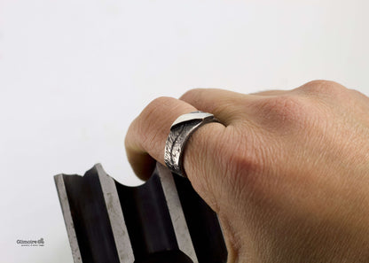 Anello a fascia in argento battuto indossato su un dito, con una finitura elegante e moderna