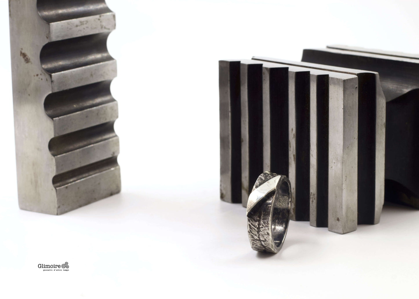 Anello a fascia in argento battuto posizionato tra attrezzi da lavoro metallici