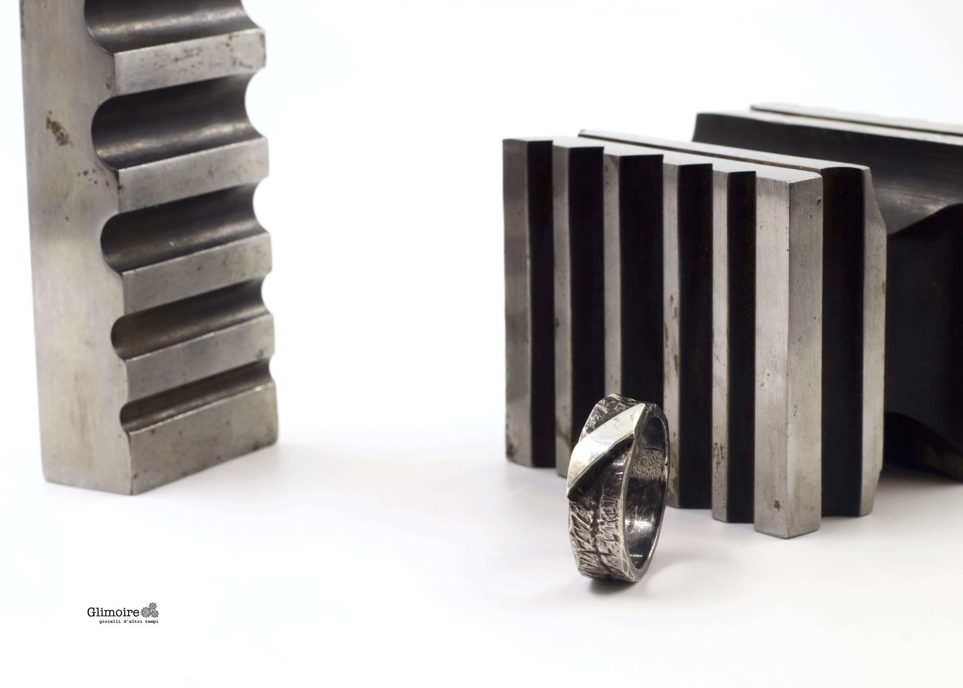 Anello a fascia in argento battuto posizionato tra attrezzi da lavoro metallici