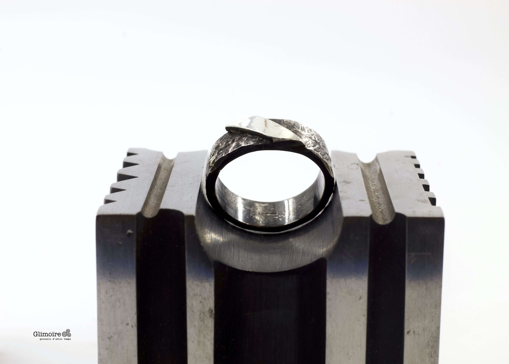 Anello artigianale Riverberi Glimoire, fascia in metallo lavorato con riflessi di luce.