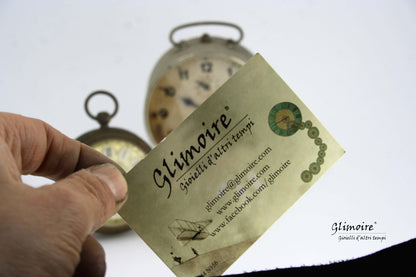 Biglietto da visita Glimoire con orologi vintage sullo sfondo, simbolo di anello con meccanismo di orologio
