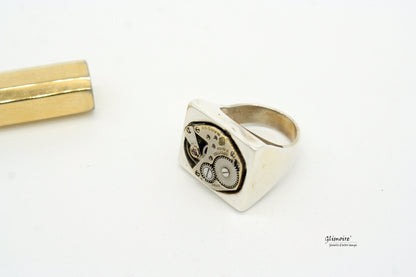 Anello in argento con meccanismo dettagliato e design unico, accanto a un oggetto dorato