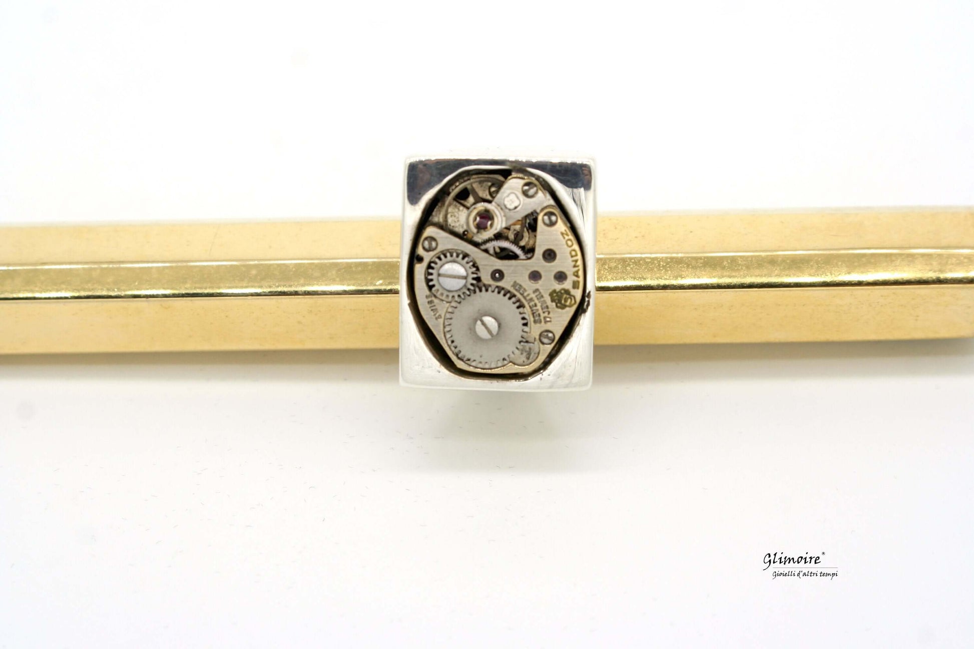 Anello in argento con meccanismo visibile in dettaglio su sfondo dorato