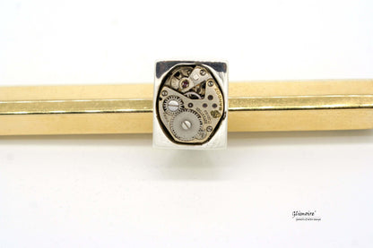 Anello in argento con meccanismo visibile in dettaglio su sfondo dorato
