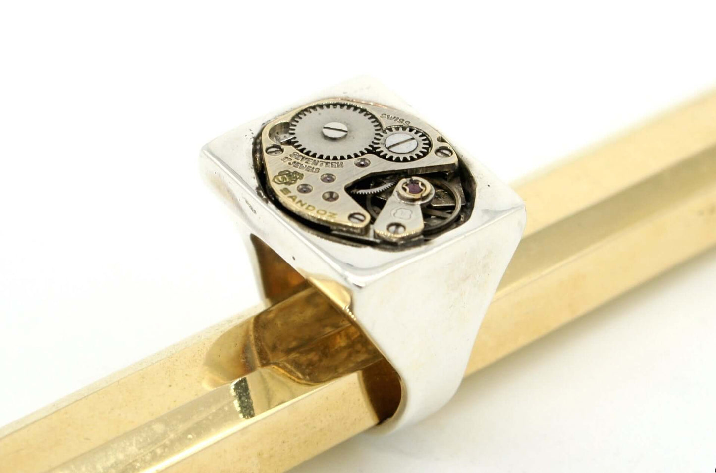 Anello in argento con meccanismo visibile e dettagli di ingranaggi su fondo chiaro