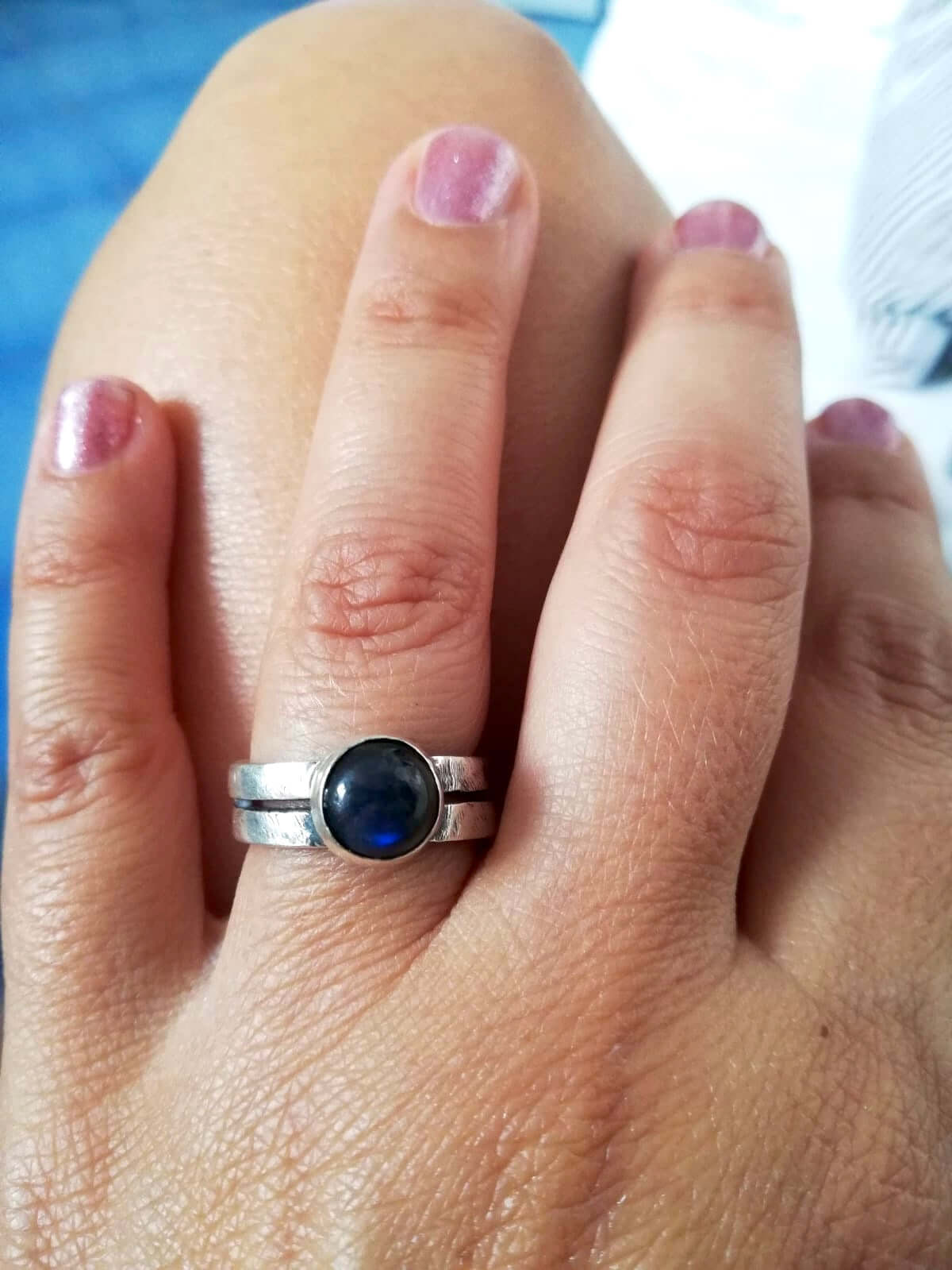 Anello intrecciato con pietra blu indossato su una mano con smalto rosa