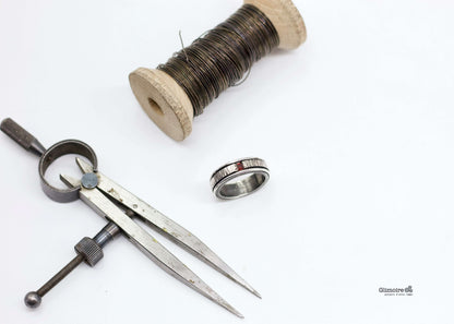 Anello maschile pietra rossa vicino a una matassina di filo e strumenti da gioielleria