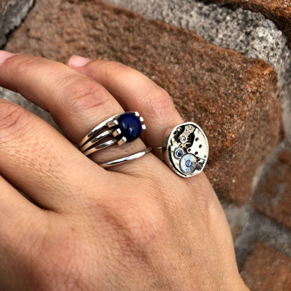 Anelli in argento con anello meccanismo di orologio e pietra blu, indossati su una mano