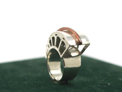 Anello metafisico moderno in metallo con design unico e dettagli in rame, visibile su sfondo verde