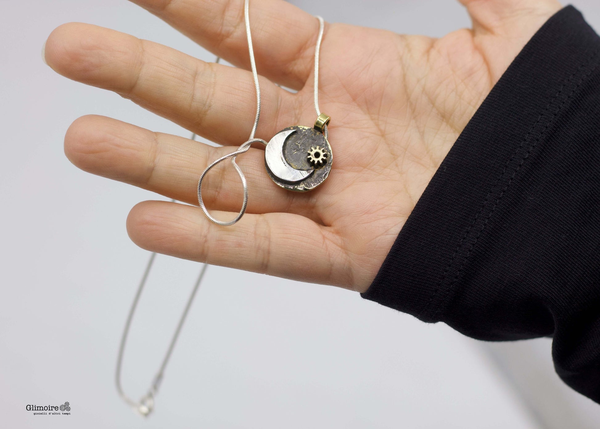 collana luna Glimoire mostrata in mano con pendente luna a mezzaluna e sole su disco metallico con catena sottile