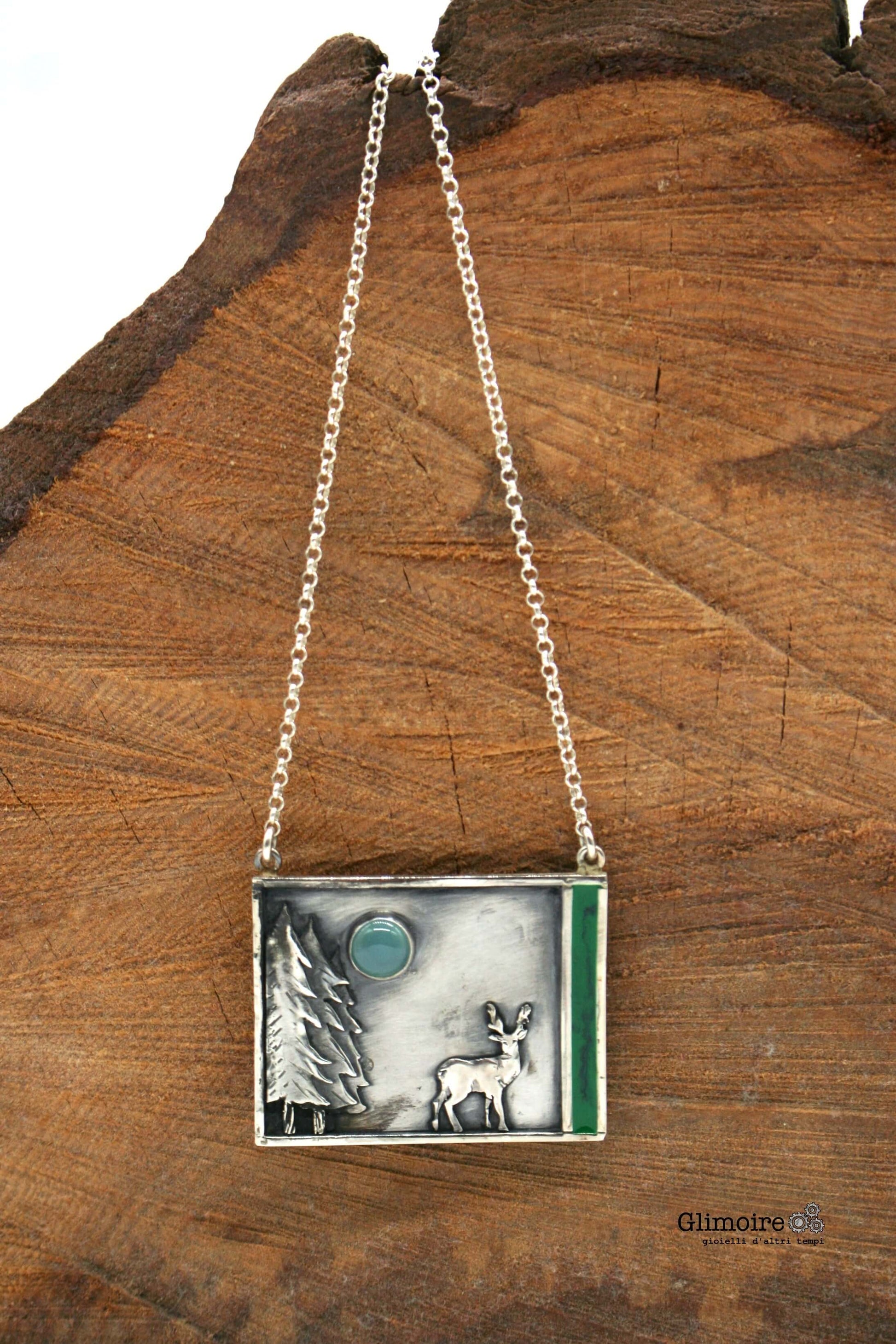 Collana lunga Habitat in argento con pendente inciso e catena adagiata su legno