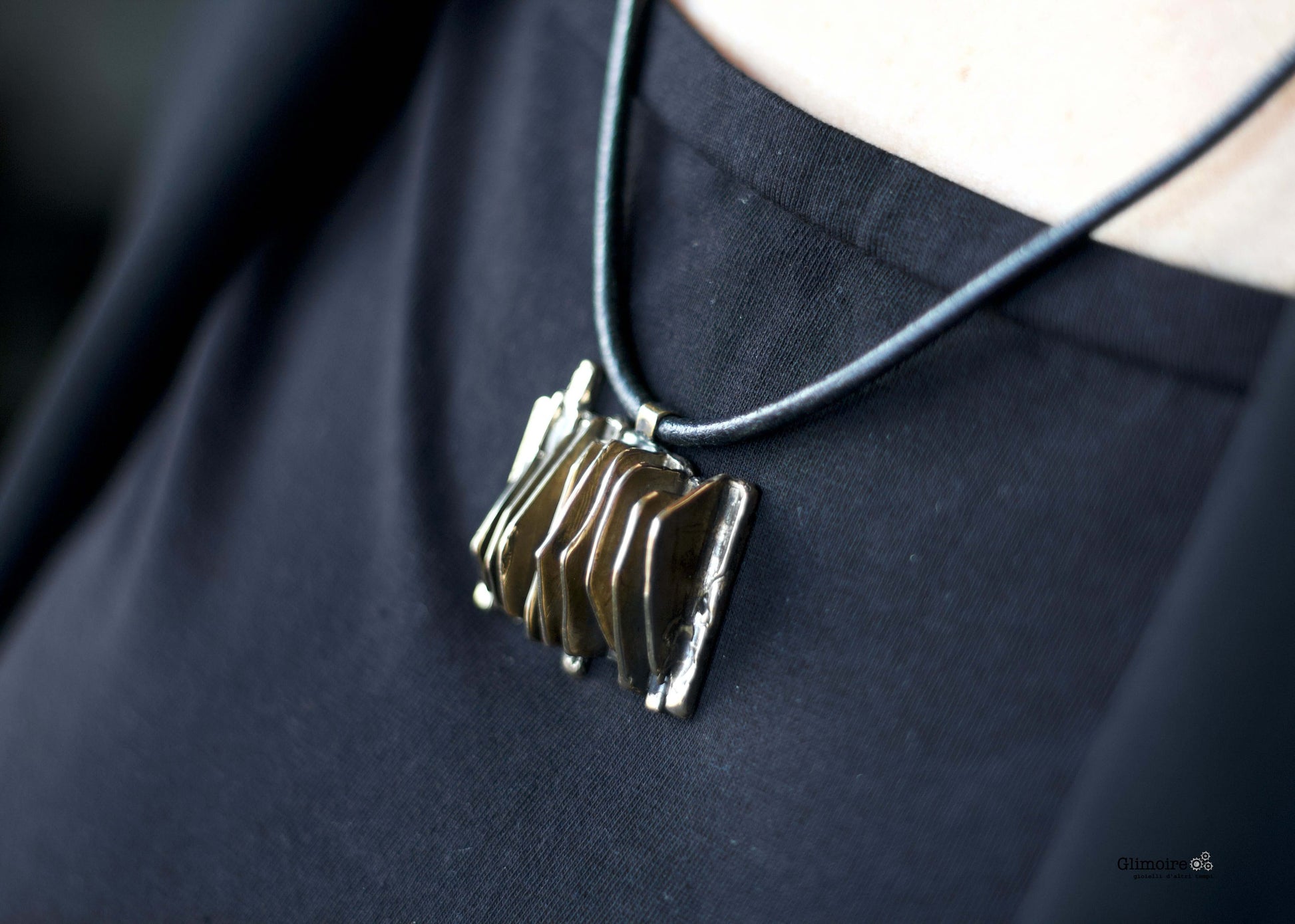 Collana Glimoire con ciondolo metallico a forma geometrica su cordino nero indossata su maglia nera