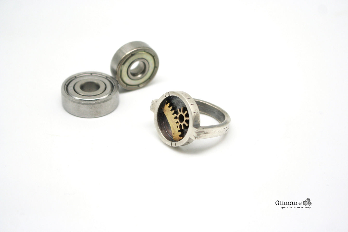 Anello tondo steampunk Glimoire con ingranaggi metallici su sfondo bianco minimalista