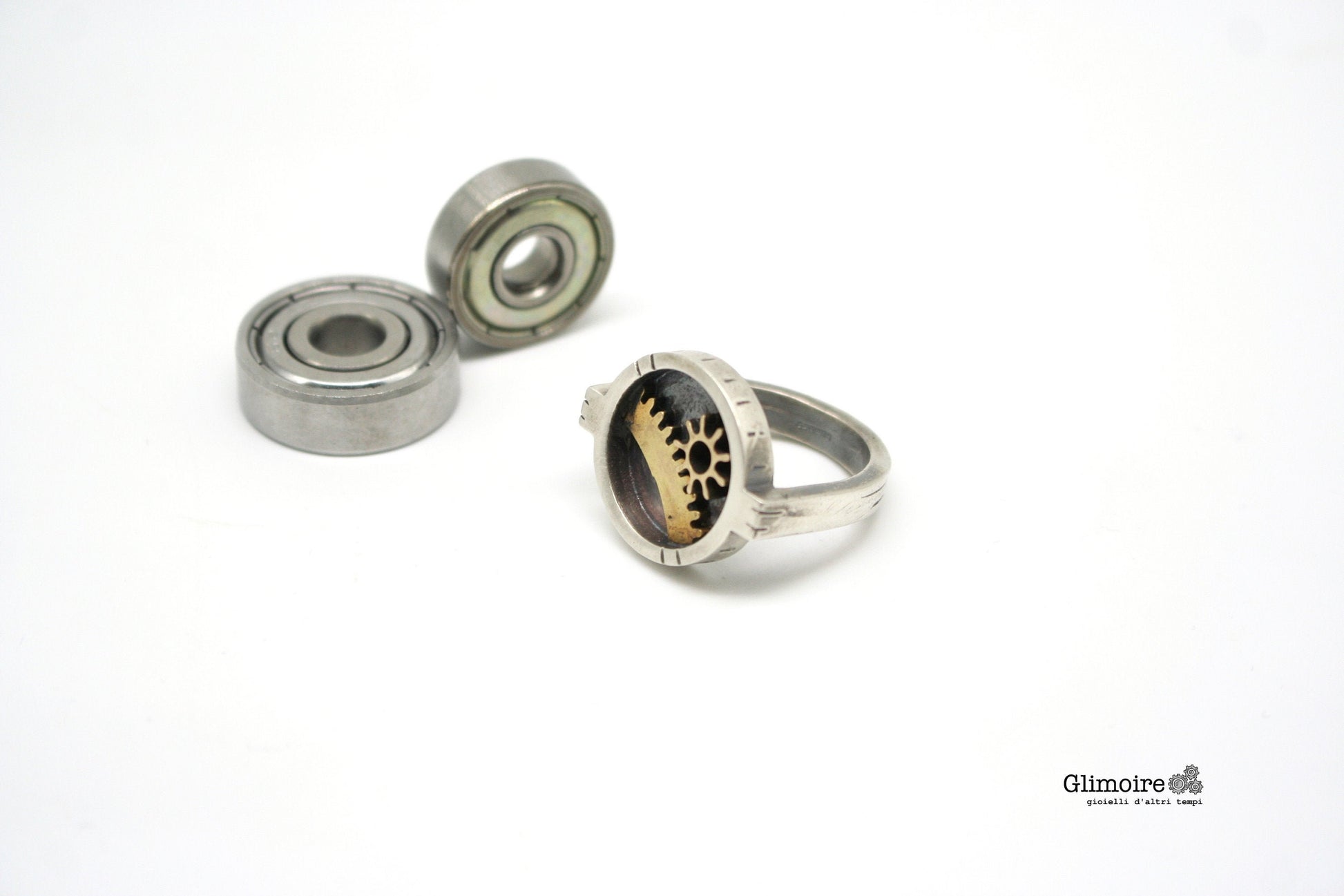 Anello tondo steampunk Glimoire con ingranaggi metallici su sfondo bianco minimalista