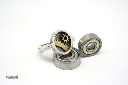 Anello industrial rettangolare Glimoire con ingranaggi in ottone su sfondo bianco