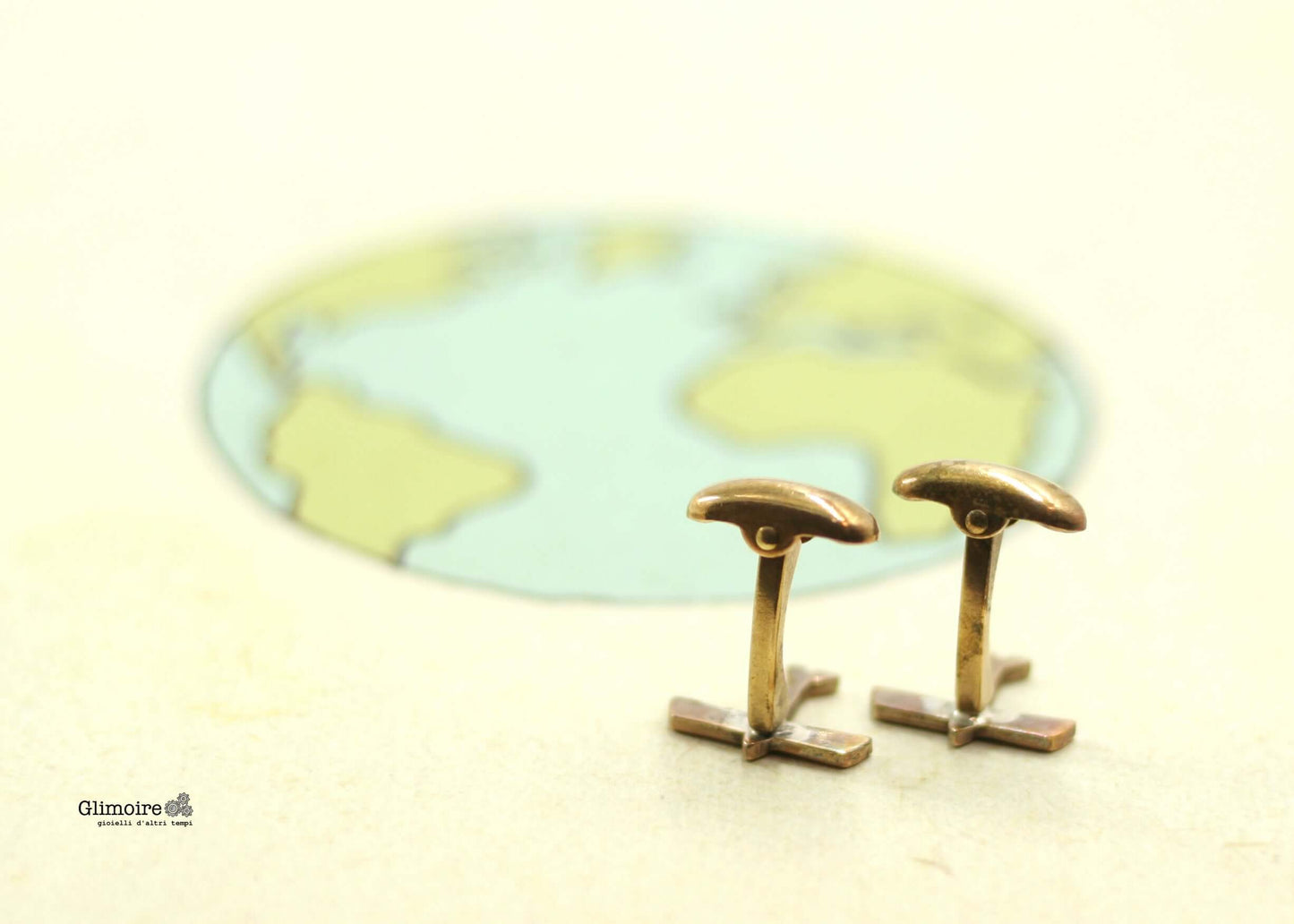 Gemelli da camicia Glimoire in ottone con design minimalista davanti a mappa del mondo sfocata