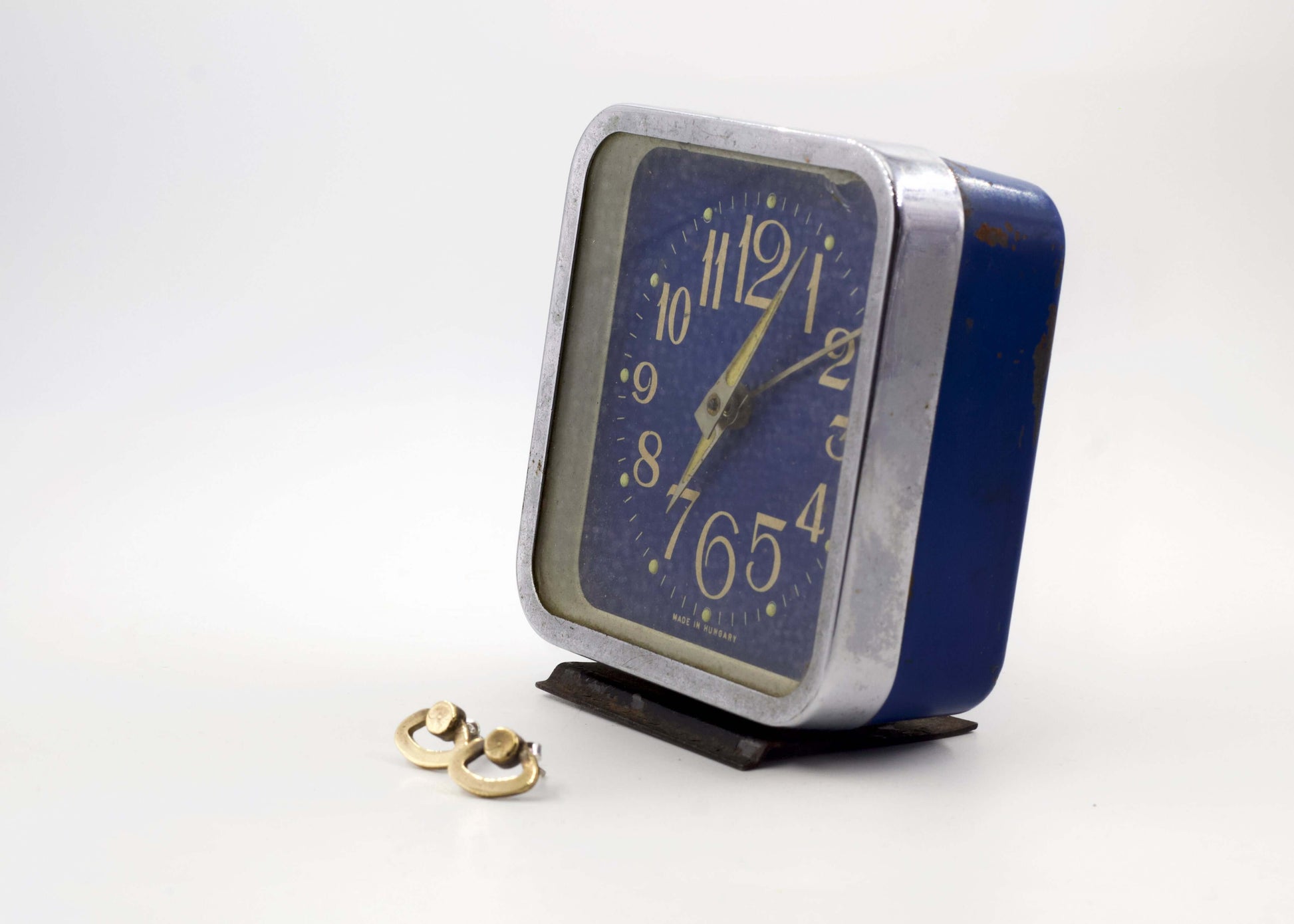 Orecchini particolari ispirati a sveglie con design originale accanto a una sveglia vintage blu