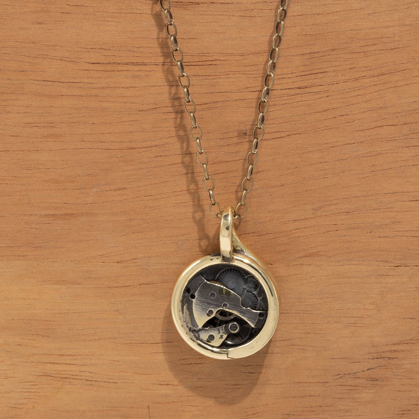 Collana Glimoire con pendente artigianale con meccanismo in metallo su sfondo legno