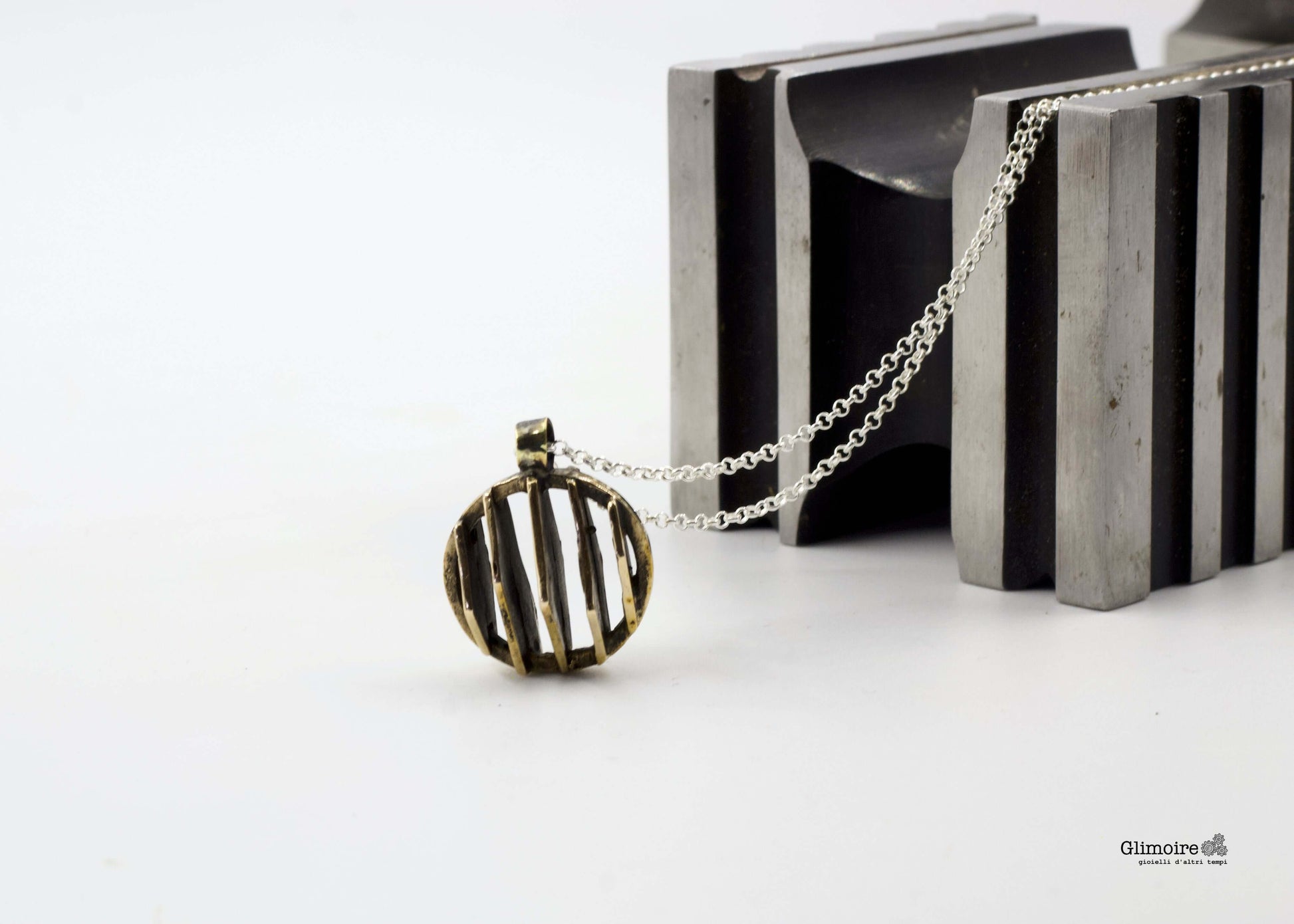 Collana con pendente dal design geometrico in bronzo appoggiata su un supporto metallico